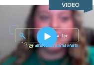 A thoughtful scene of a child seated at a desk with long hair and casual clothing, leaning forward while looking down at their work. The setting appears warm and home-like, suggesting a quiet moment of reflection or emotional expression.